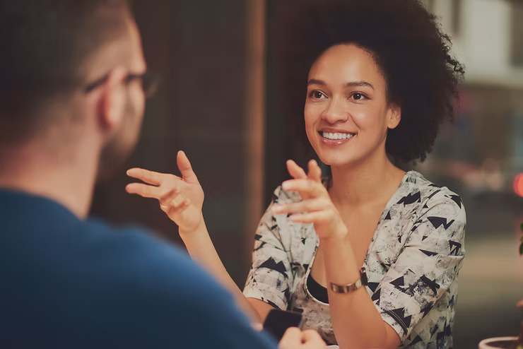 A woman gestures and smiles during conversation with a listening man.