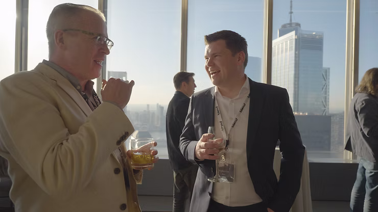 Two C-suite professionals talk at a Blend community networking event, wearing Blend branded lanyards. They hold drinks.