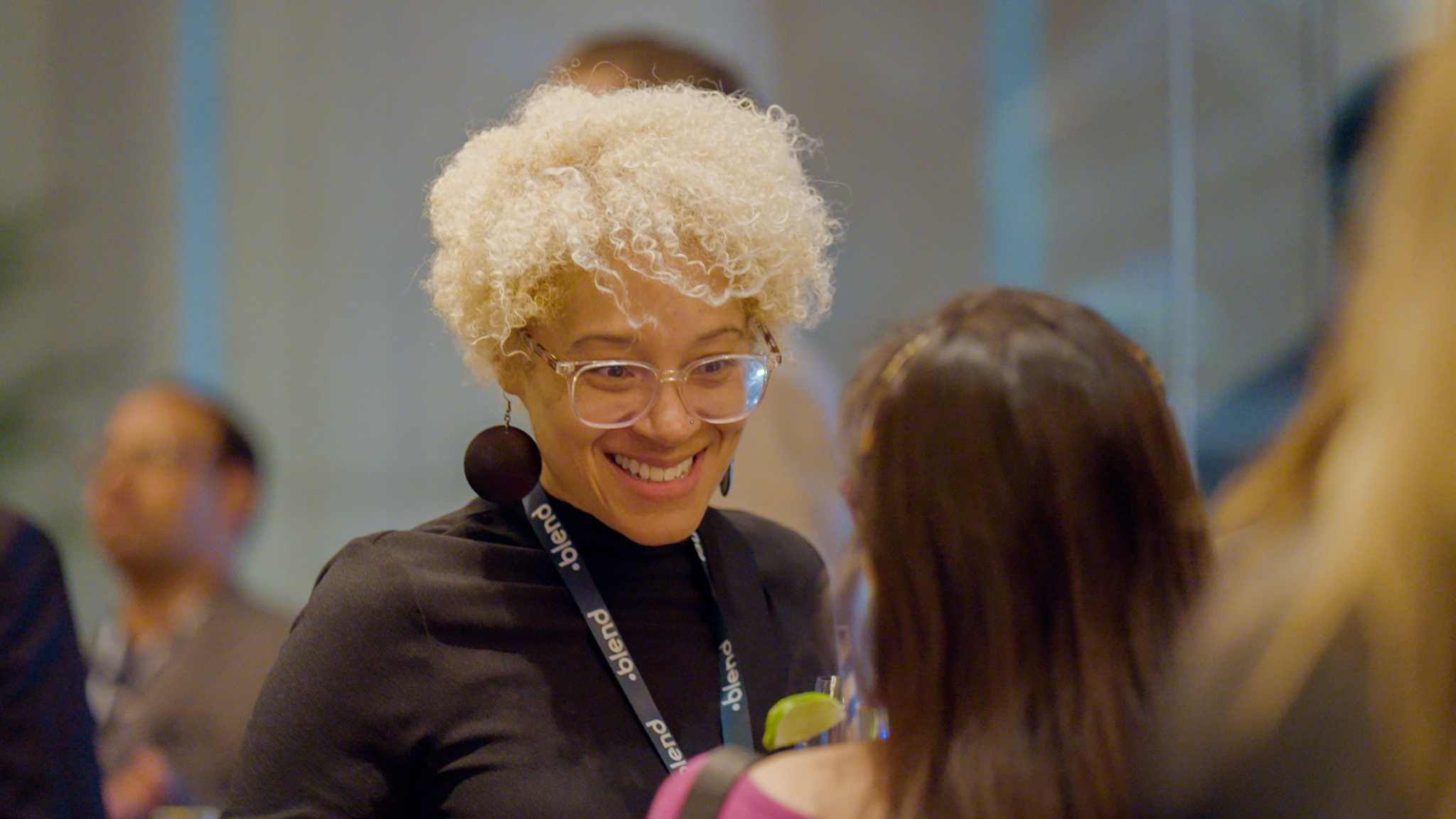 A C-suite professional enjoys a conversation at a Blend community networking event. They wear a Blend branded lanyard.