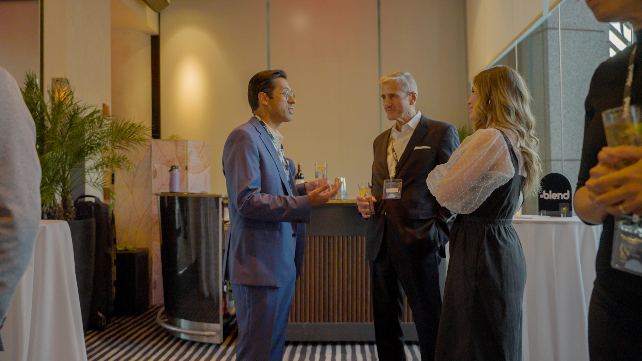 A group of three C-suite professionals talk at a Blend community networking event, wearing Blend branded lanyards.