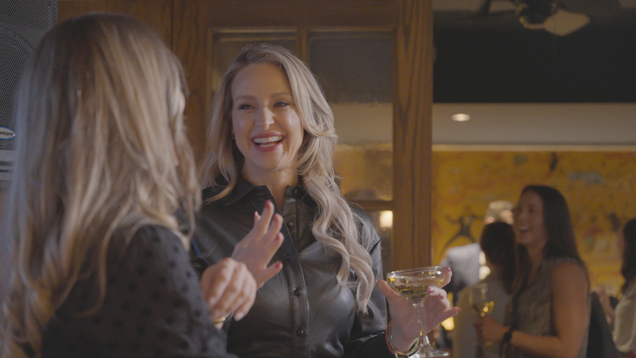 Two C-suite professionals talk at a Blend community networking event, wearing Blend branded lanyards. One holds a glass of champagne.