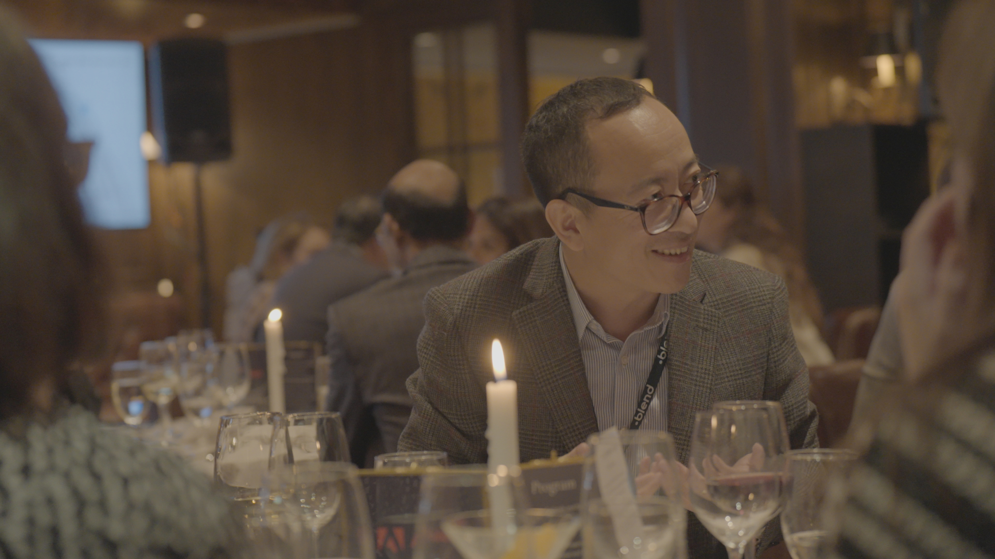 A C-suite professional enjoys a Blend community networking event, wearing a Blend branded lanyard. He is seated.