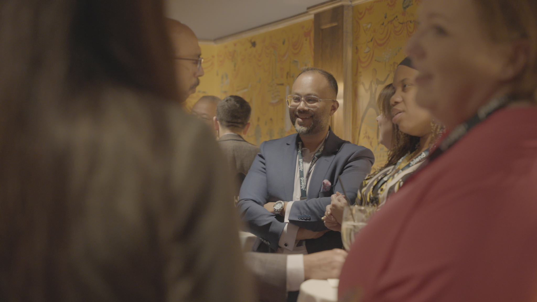 A group of business-wear dressed C-suite professionals talk at a Blend community networking event, wearing Blend branded lanyards.
