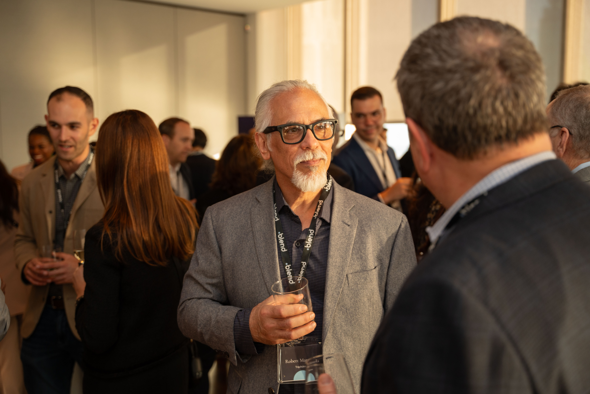 A group of C-suite professionals engage in conversation at a Blend community networking event. They wear Blend lanyards.
