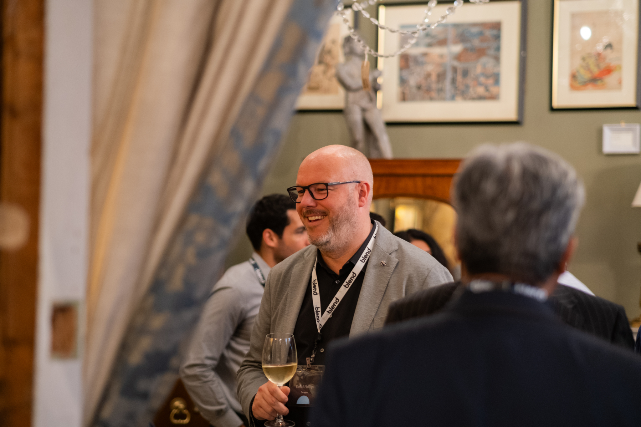 A business-wear C-suite professional enjoys a Blend community networking event. He wears a Blend branded lanyard.