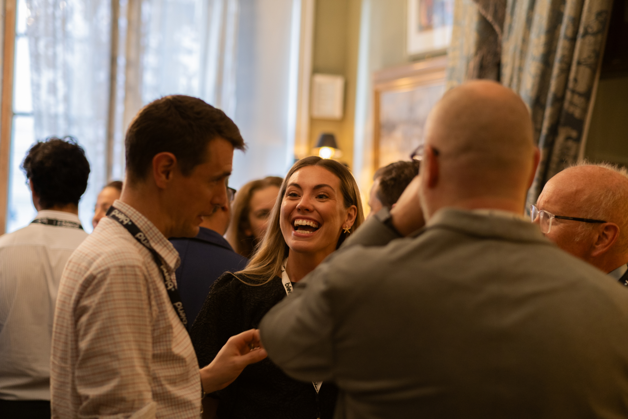 A group of business-wear dressed C-suite professionals talk at a Blend community networking event, wearing Blend branded lanyards.