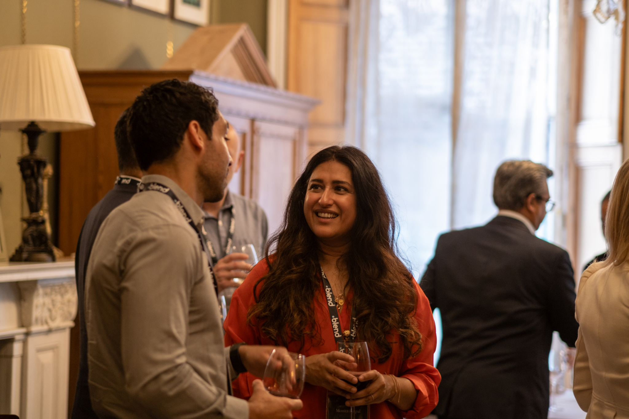 A group of business-wear dressed C-suite professionals talk at a Blend community networking event, wearing Blend branded lanyards.