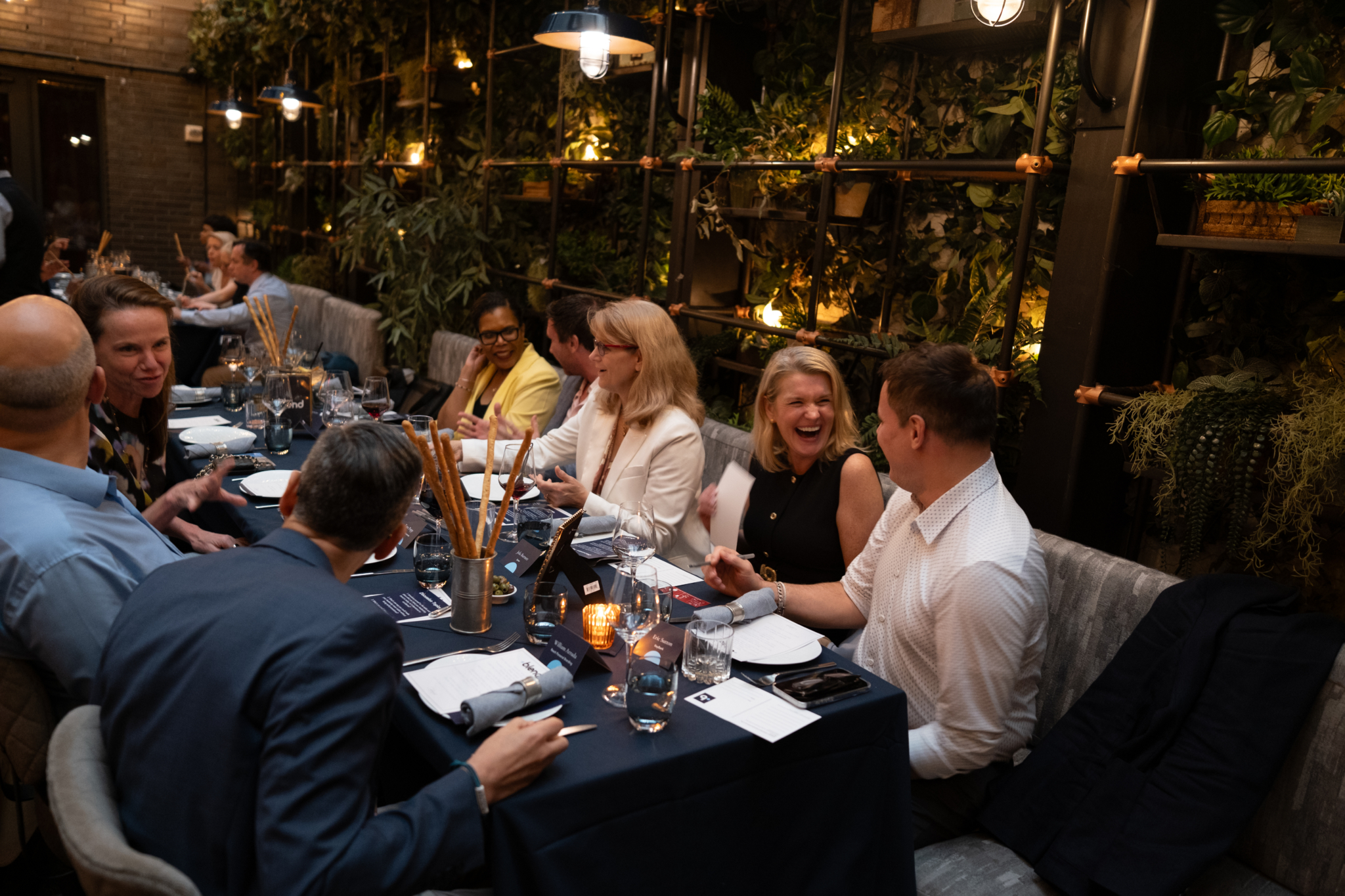 A group of seated C-suite professionals enjoy a Blend community networking event. They are sat at a long dining table.