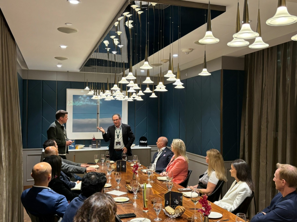 A small room of C-suite professionals sit at a long table and listen to a guest speaker talk at a Blend event.
