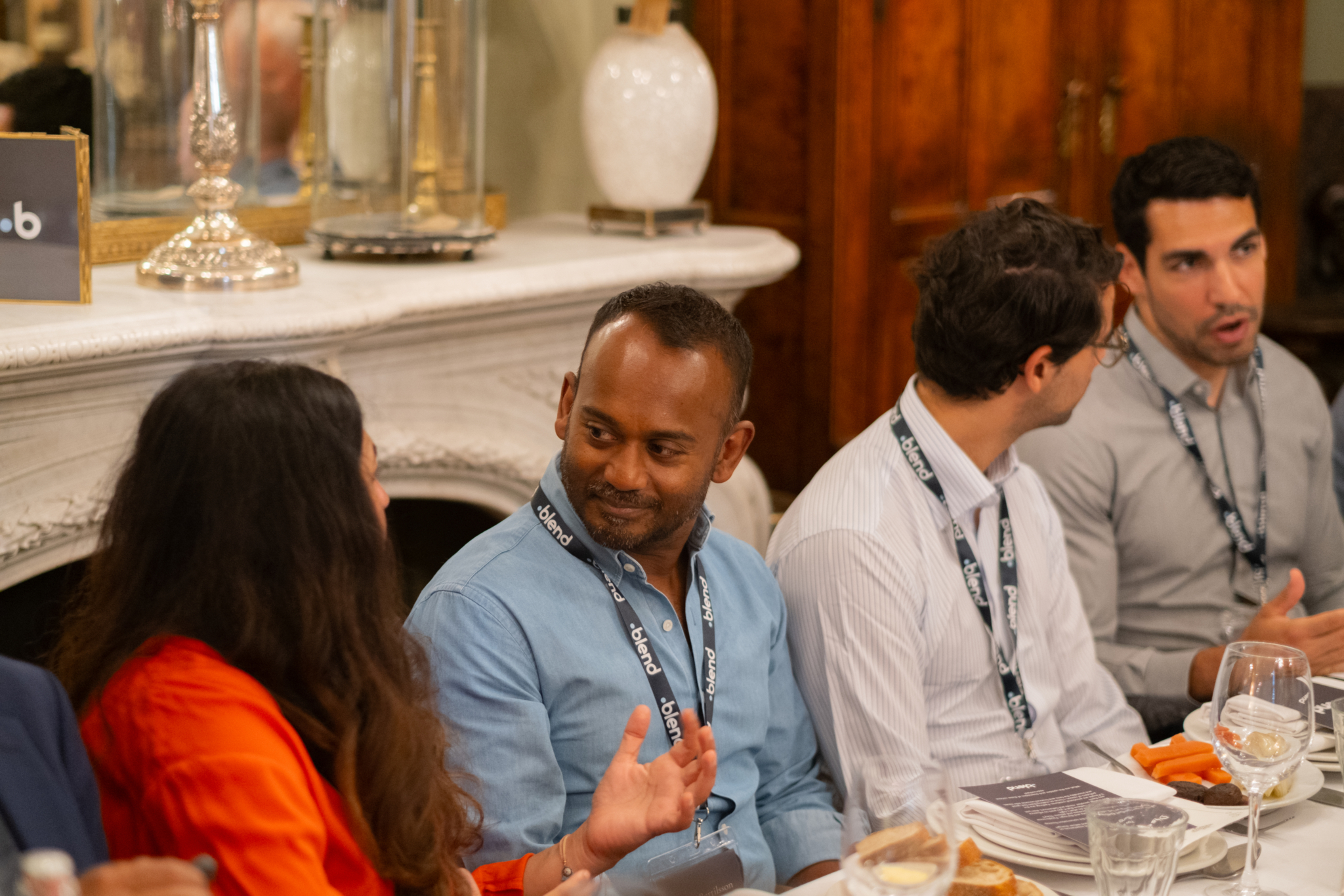 A group of seated C-suite professionals enjoy a Blend community networking event. They are sat at a long dining table.
