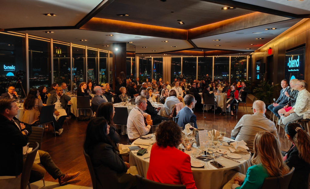 A room of C-suite professionals sat at round tables listen to a panel talk at a Blend community networking event.