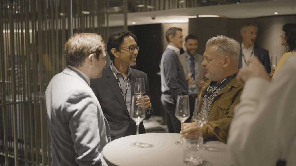 A group of C-suite professionals talk at a Blend community networking event. They hold glasses of fizz.